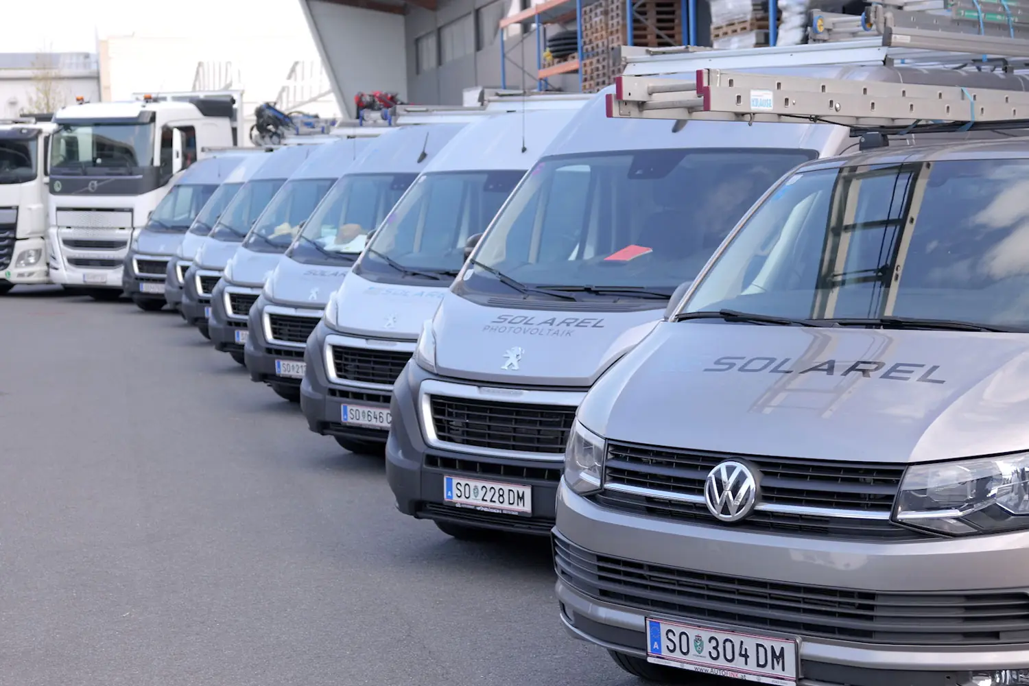Fahrzeugflotte von Solarel: Transporter und LKW mit Solarel-Beschriftung vor der Halle